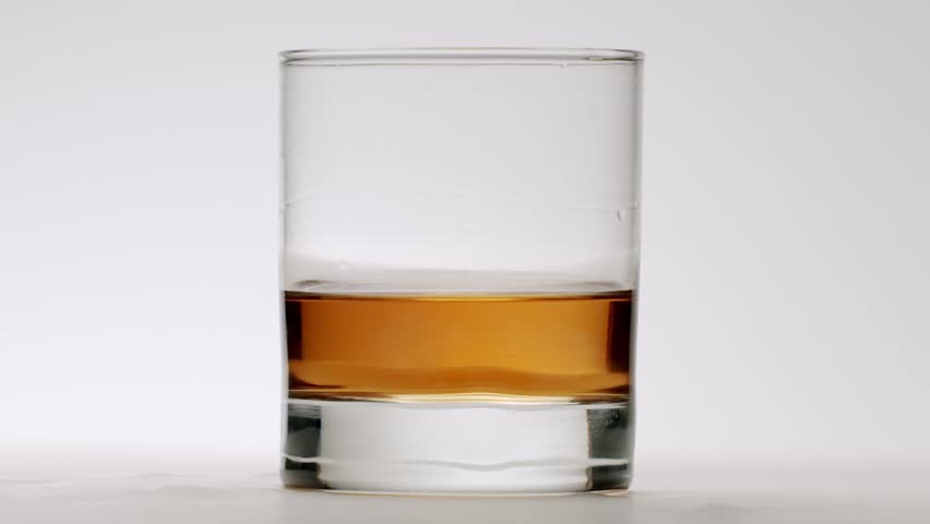 Slow motion video of crystal clear ice cubes dropping into a rocks glass filled with golden brown whiskey, creating a dramatic splash and swirl, isolated on a clean white background