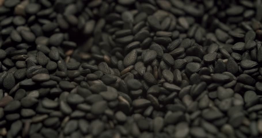 Super slow motion shot of black sesame seeds filling a wooden bowl isolated on a white background, Slow motion footage of a small wooden bowl full of black sesame seeds rotating on a white background