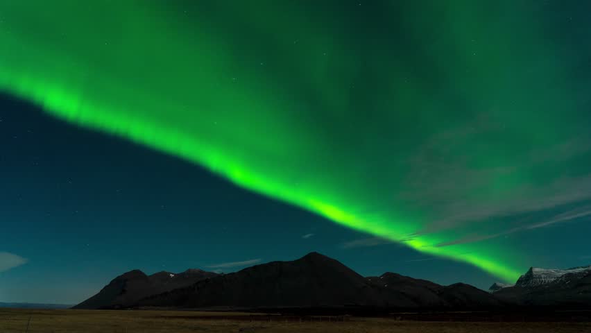 Spectacular green aurora borealis, also known as northern lights, dancing across the night sky above a dark Arctic landscape. Bright stars visible in the background, breathtaking natural phenomenon and celestial display.