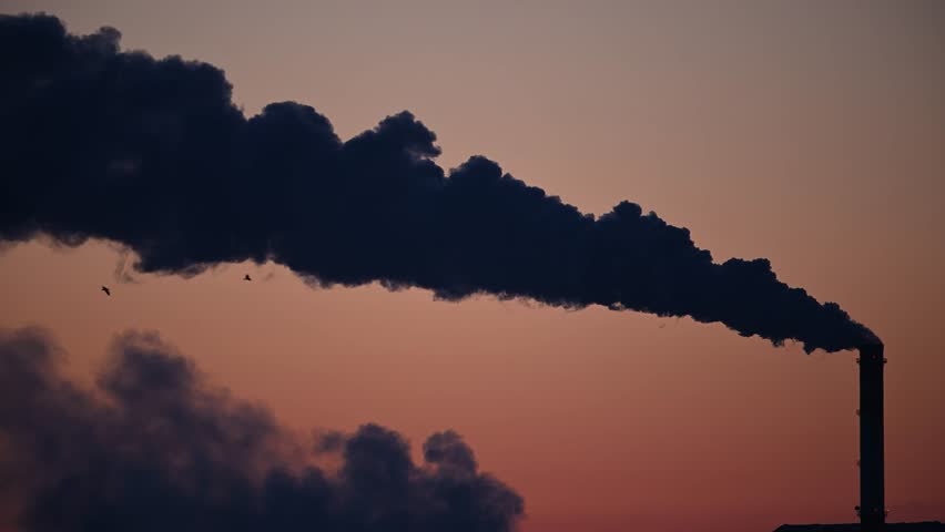 Smoke from a production chimney against the backdrop of the sunset sky.