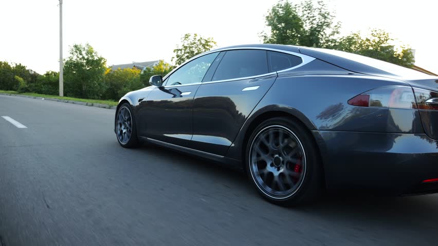 Modern electrical automobile driving at urban road on sunny day. Electric vehicle riding through empty highway. Ecology friendly car riding moving along motorway. Concept of green innovation. Slow mo