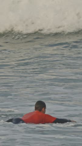 An adult man in an orange T-shirt swims into the sea lying on a surfboard
