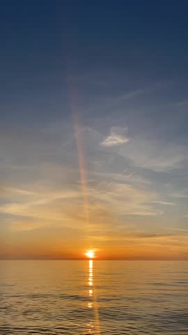 Vertical seascape timelapse video with sun setting over ocean horizon, golden reflection on rippling water under colorful sky