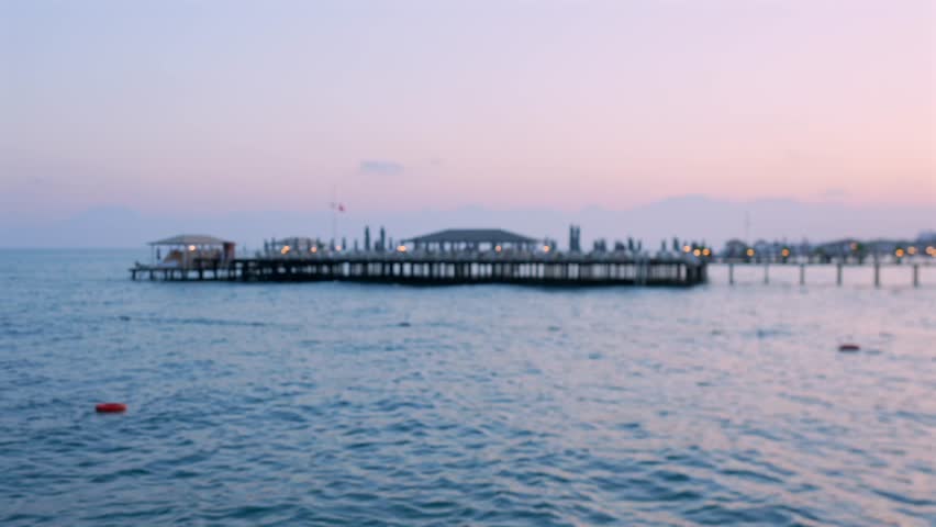 Mediterranean sea at dusk with calm water city lights and distant long pier