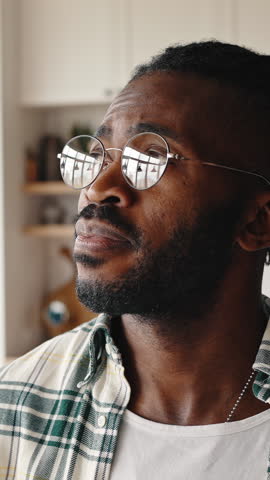 Close up portrait of positive african american guy wearing eyeglasses turning face to camera and smiling, posing at home interior, slow motion
