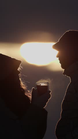 Silhouette of girlfriend shares cup of hot tea with boyfriend at winter sunset