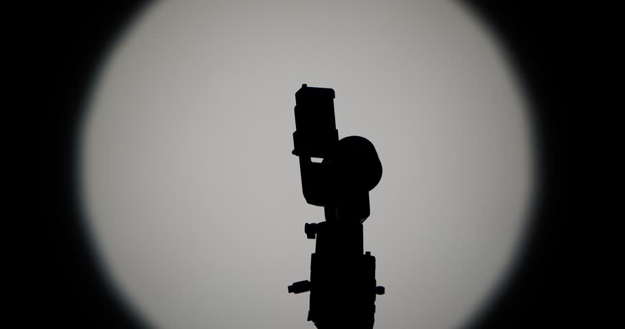 The operator sets up and connects the camera to a motorized stabilizer with a suspension, filming against a bright round light on a dark background, symbolizing film production.