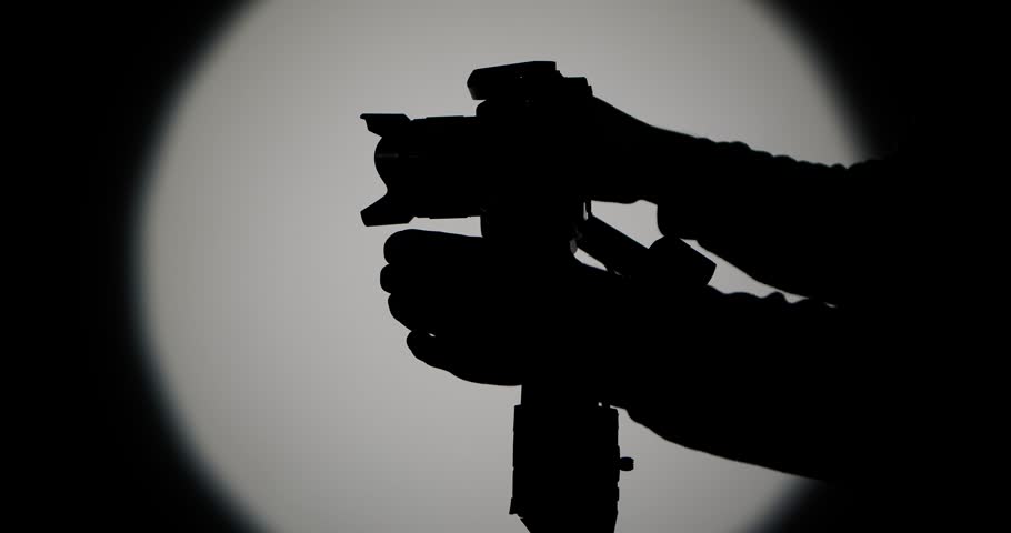 The operator sets up and connects the camera to a motorized stabilizer with a suspension, filming against a bright round light on a dark background, symbolizing film production.
