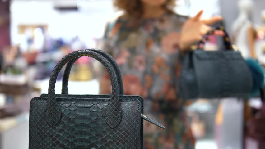 Fashionable woman browsing in a luxury boutique, comparing an exclusive snakeskin handbag with another purse in her hand, with the focus on the designer python leather accessory in the foreground