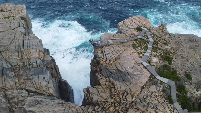 Forward-moving drone shot advancing from rocky terrain toward the dramatic coastal cliffs of The Gap in Torndirrup National Park, Western Australia. Powerful Southern Ocean waves crash against steep granite formations, creating an intense and cinematic seascape along the rugged coastline near Albany.
