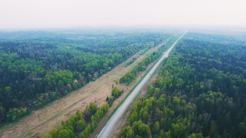 Aerial view of a long road through a dense forest landscape