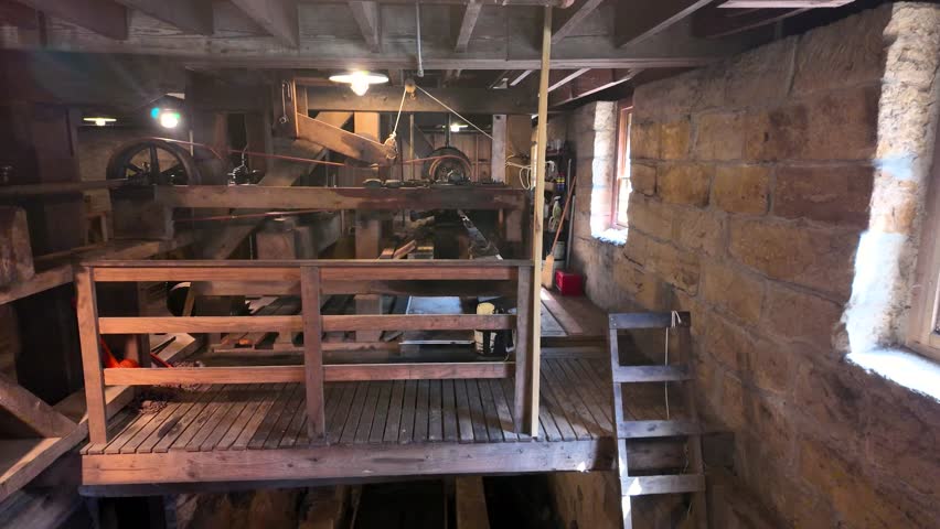 Wooden gears and wheels turning inside an old gristmill with stone walls and wooden structures inside  Lanterman