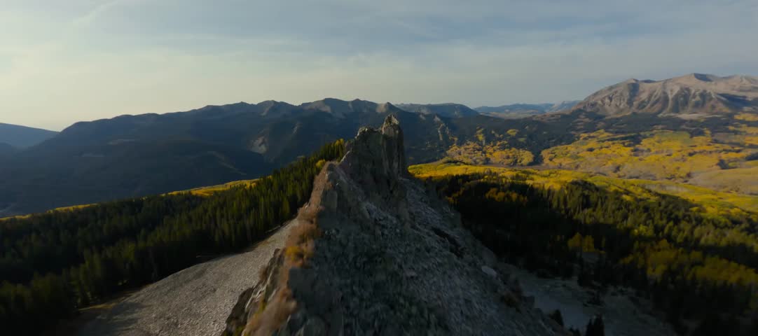 Intense FPV drone flyover skimming inches above the sharp rocks of a mountain ridge. The shot emphasizes the raw texture of the stone and the vertigo-inducing height above the autumn-colored slopes.