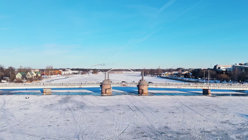 Drone view of the historic Pärnu city center bridge crossing a frozen river in bright winter sunlight. Calm urban landscape, architecture and seasonal Baltic atmosphere.