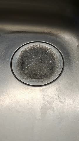 Increasing dish soap foam overflowing from a stainless steel kitchen sink drain. Vertical UHD video showing white suds and metallic shine. Perfect for plumbing services.