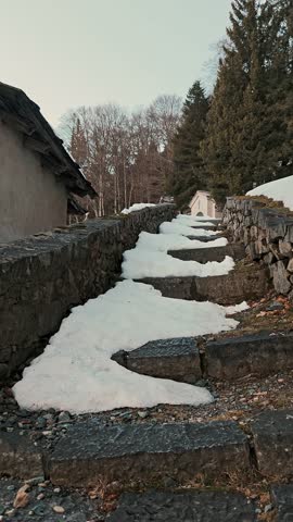 Snow-covered stone steps lead up a path along an old wall near a historical site.