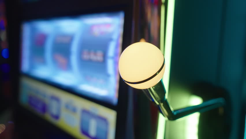 Casino gambling scene with hand pulling slot machine handle. Bright neon reflections and shallow focus create intense moment of risk and chance.