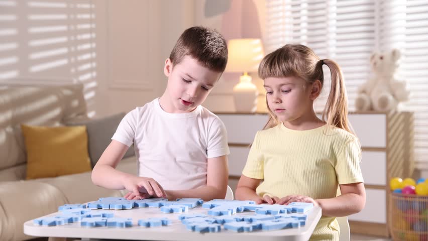 Little brother and sister playing with puzzles at white table indoors