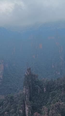 Cinematic aerial shot looking down at the unique sandstone pillars of Zhangjiajie covered in winter snow, with thick mystical fog drifting in the foreground. Hunan, China.