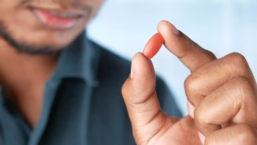 Close-up slow motion shot of person holding a single red pill between fingers