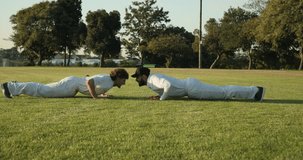 Diverse male partners alternating pushup handclasps on grass by orange cones for balance training. Athletic, teamwork, coordination, fitness, outdoor, strength, motivation - Powered by Shutterstock - Get 15% off with code: PIKWIZARD15