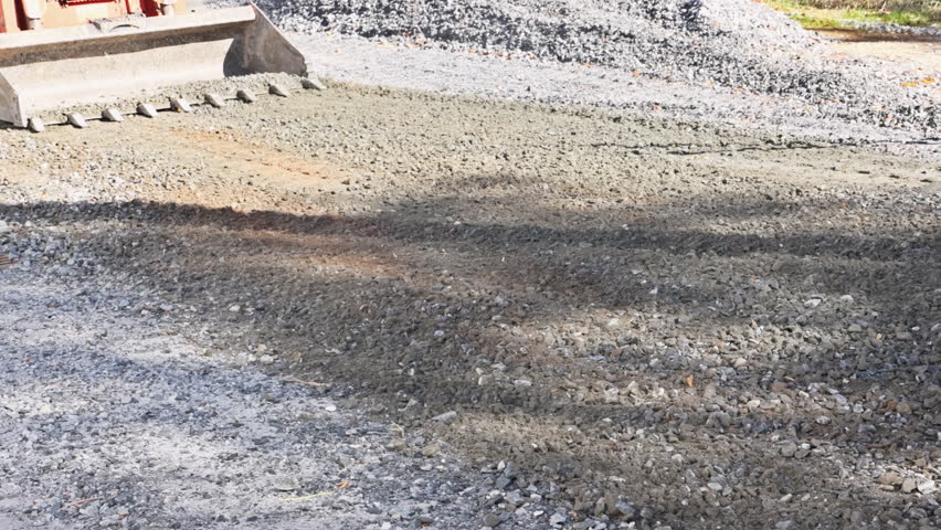 Construction machinery is working hard to spread gravel on site next to road