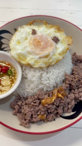 Thai style minced meat served with steamed rice and fried egg, accompanied by spicy chili fish sauce. Popular street food dish in Thailand, simple and authentic Asian comfort meal.