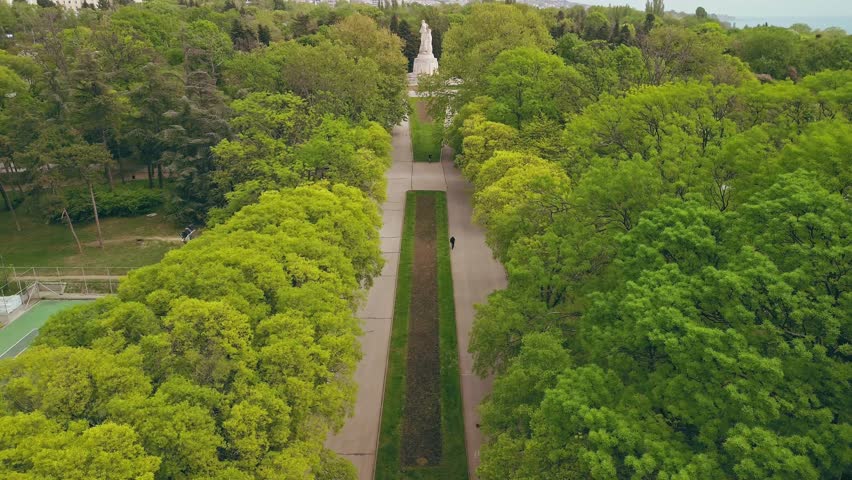 Aerial top-down view of a long walking path through a lush green city park with sports courts and tall trees