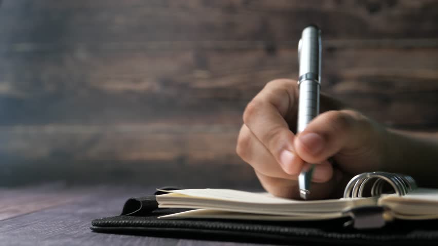 Close-up of hand holding pen and writing in notebook, business and education concept