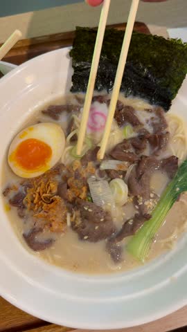 Japanese style beef ramen served with soft boiled egg, noodles, seaweed and fresh toppings in creamy broth. Traditional Asian comfort food enjoyed at restaurant.