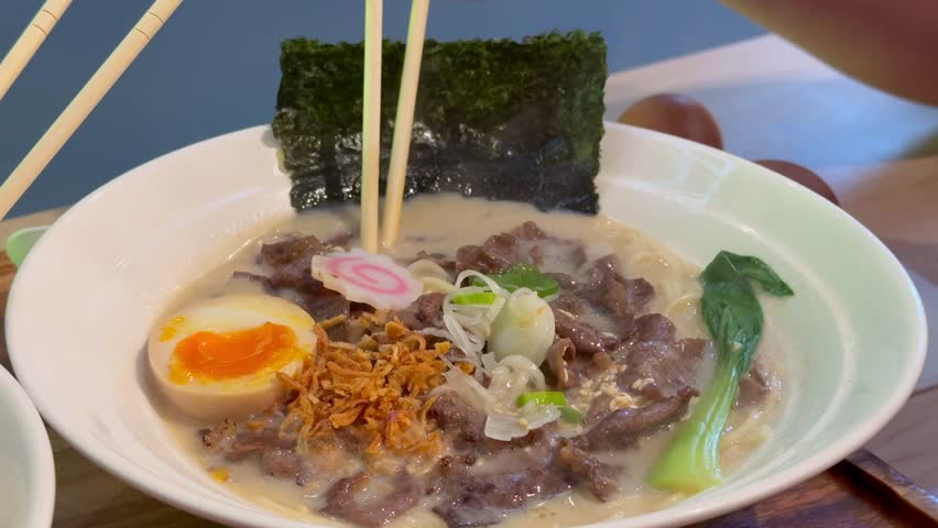 Japanese style beef ramen served with soft boiled egg, noodles, seaweed and fresh toppings in creamy broth. Traditional Asian comfort food enjoyed at restaurant.
