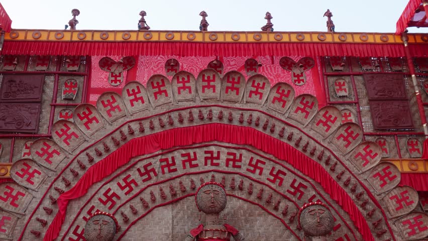 Elaborately decorated red bamboo craft arch with tribal figures and swastika symbols