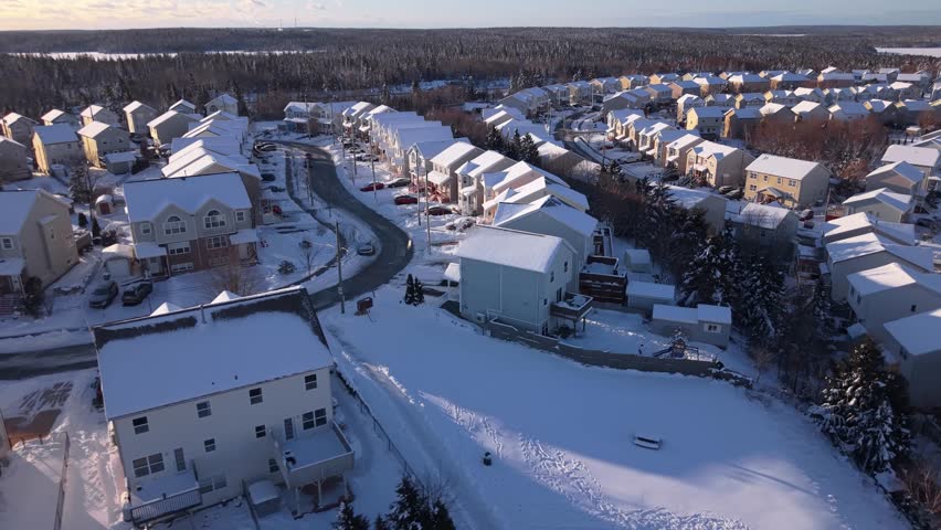 Cinematic drone shot over snow-covered cottages and rooftops in Beachville suburb of Halifax after winter storm. Residential community blanketed in white snow under sunny winter sky,Nova Scotia,Canada