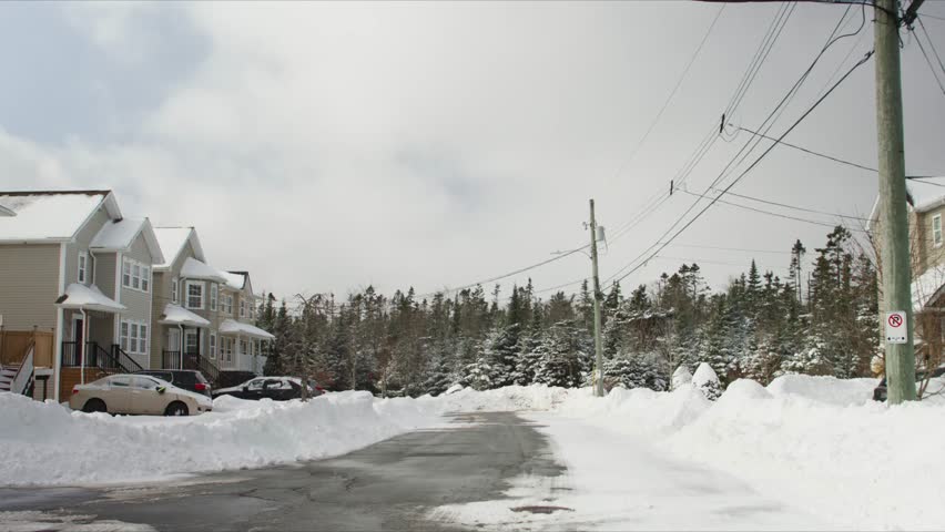 Beechville near Halifax: thick snow blankets private homes, yards and streets. Local residents go outside to shovel snow and clear paths, bright daylight shows typical Nova Scotia snowstorm recovery.