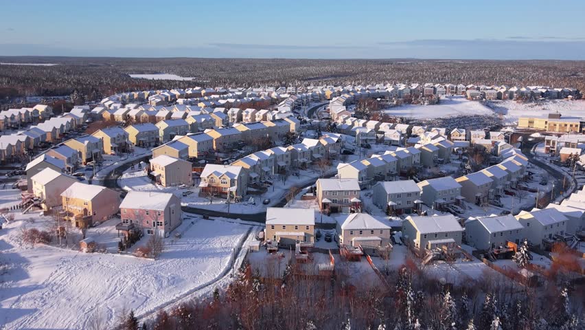 Drone aerial footage after overnight snowfall: even snow layer on roofs and streets of private homes in Beechville near Halifax. Bright winter day in Nova Scotia, Canada, peaceful snowy suburb.