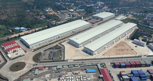 Forward aerial view of a large industrial complex featuring long warehouse buildings, a gantry crane, and stacked shipping containers. - Powered by Shutterstock - Get 15% off with code: PIKWIZARD15