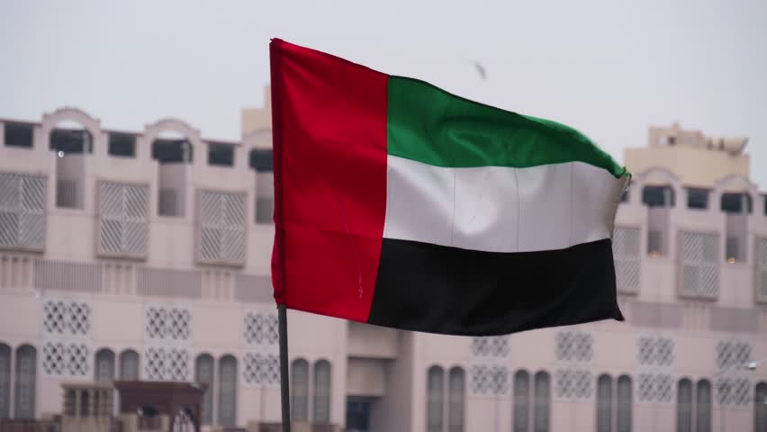 UAE flag waving before Old Dubai buildings in Dubai, United Arab Emirates
