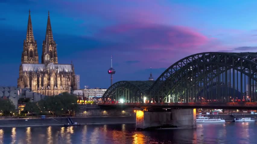 Cologne Cathedral and Hohenzollern Bridge at dusk, showcasing iconic German architecture, river reflections, and scenic city skyline.