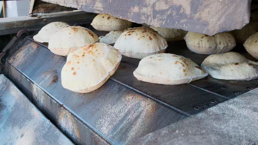Close-up footage of traditional egyptian flatbread aish baladi baking in conveyor oven. Baking pita bread on traditional egyptian street baker shop