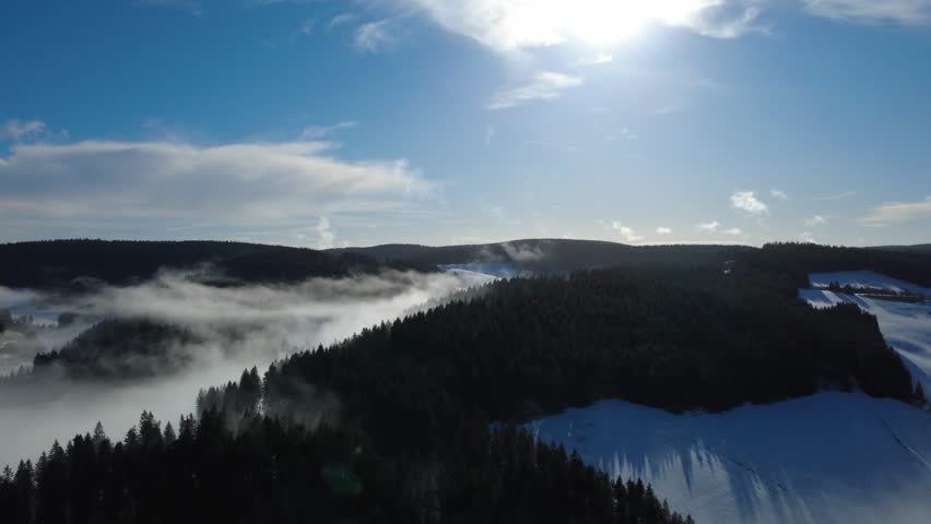 Cinematic aerial view of winter fog rolling over the Black Forest mountains in Germany. Snow-covered hills and forest create a dramatic natural landscape. Ideal footage for travel, nature, atmosphere, and seasonal backgrounds.