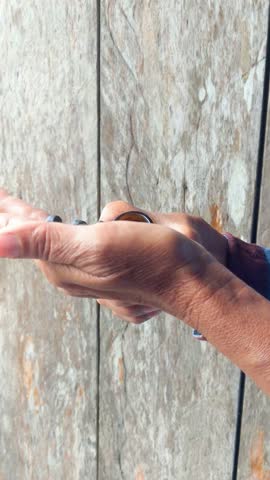 Close up of person pouring natural essential oil or herbal medicine from an amber glass bottle into their palm, rustic wooden background