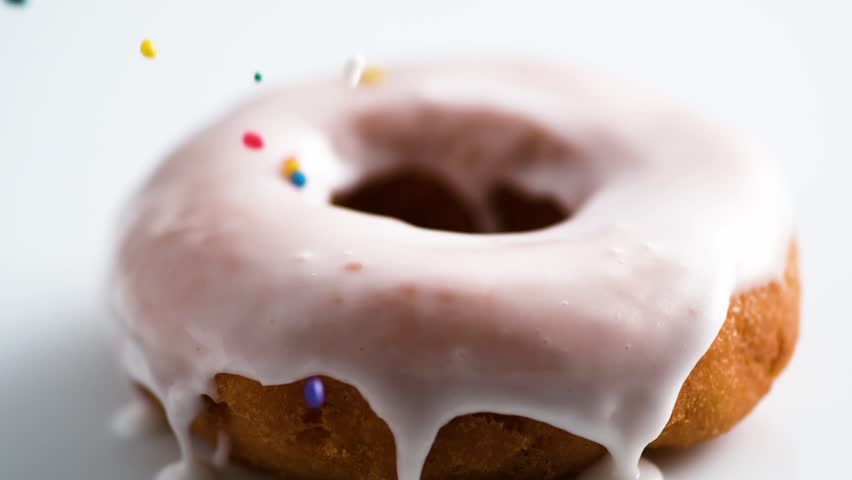 Top view of a chef decorating a donut with rainbow sprinkles. Professional pastry decoration process on a clean, bright background.