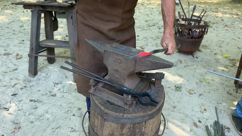 Blacksmith hammers glowing hot iron on anvil, close up