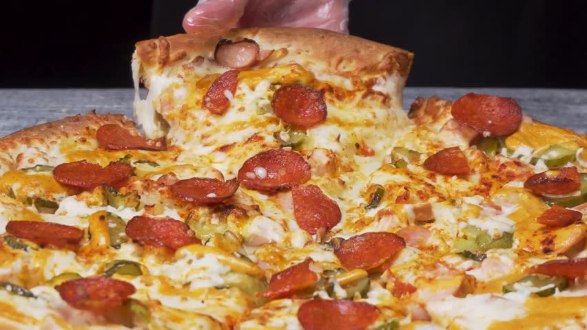 Close-up of a hand taking a slice of pizza with stretching mozzarella on a black background, perfect for food, cooking, and culinary visuals.