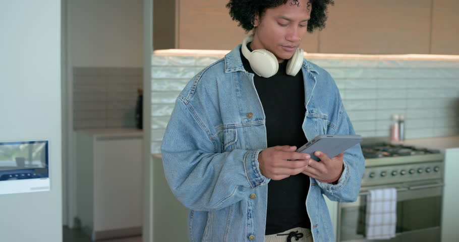At kitchen island, mid adult African American man scrolling tablet then typing on laptop for work. Technology, workspace, contemporary, productivity, lifestyle, communication, interior