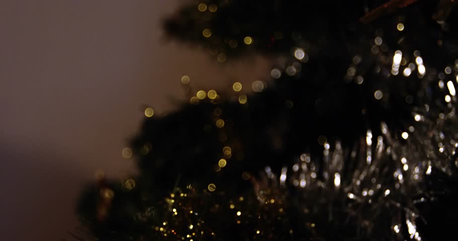 A close-up of the decorations on a christmas tree, with an animation of the text merry christmas in black letters with a bell and other decorations on a white background.