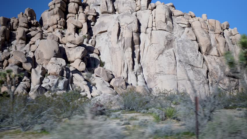Enjoy passing views of Joshua Tree National Park while driving through the park on a clear day with diverse rock formations and trees.