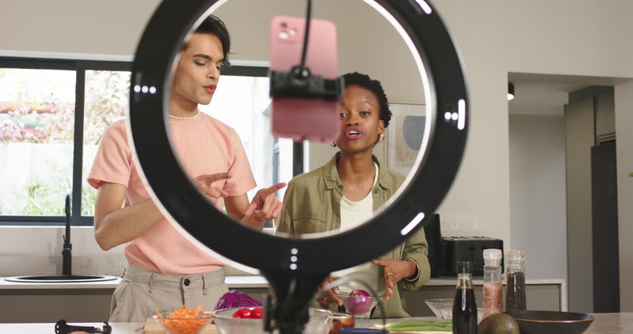 Diverse co-hosts initiating cooking tutorial by adjusting camera setup and slicing onion in kitchen. Cooking, collaboration, kitchen, lifestyle, vibrant, education, healthy