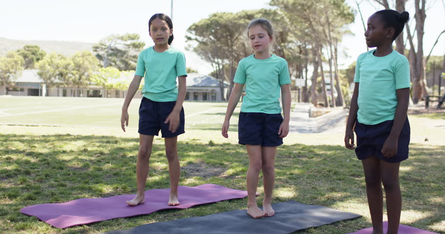 African American preteen girls in teal shirts pausing then doing lunges together on mats during PE. Outdoor, fitness, youth, coordination, balance, teamwork, field