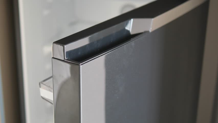 Modern gray refrigerator door opening slowly in bright kitchen showing empty shelves inside